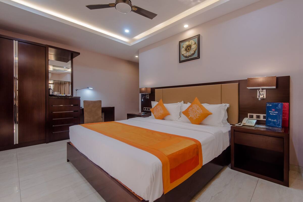 A hotel room with a large bed, a wardrobe, a nightstand with a lamp, and a ceiling fan.