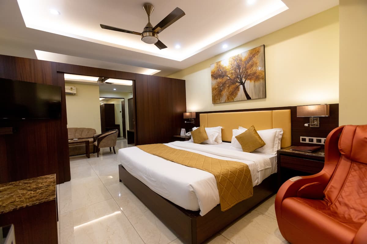 A modern hotel room with a large bed, a massage chair, a flat-screen TV, and a ceiling fan.