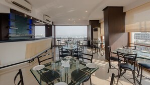 Uma zona de refeições moderna com mesas e cadeiras de vidro, um balcão de cozinha com copos e uma vista para a cidade.