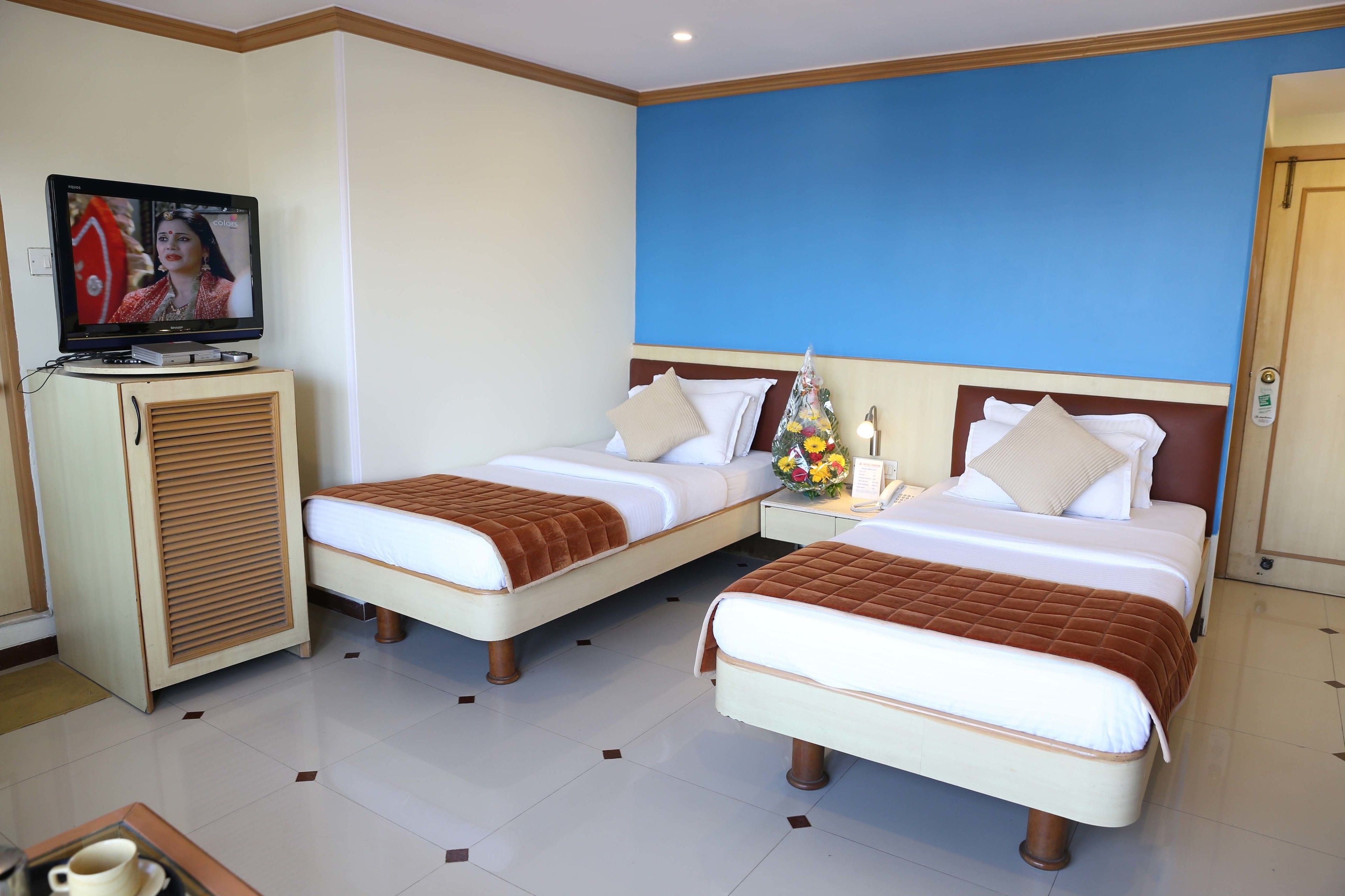 A hotel room with two beds, a television, a cabinet, and a nightstand with a vase of flowers.
