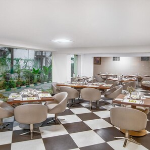 A modern dining area with checkered flooring, contemporary chairs, and tables set for dining. - Monarch Luxur (Bengaluru)