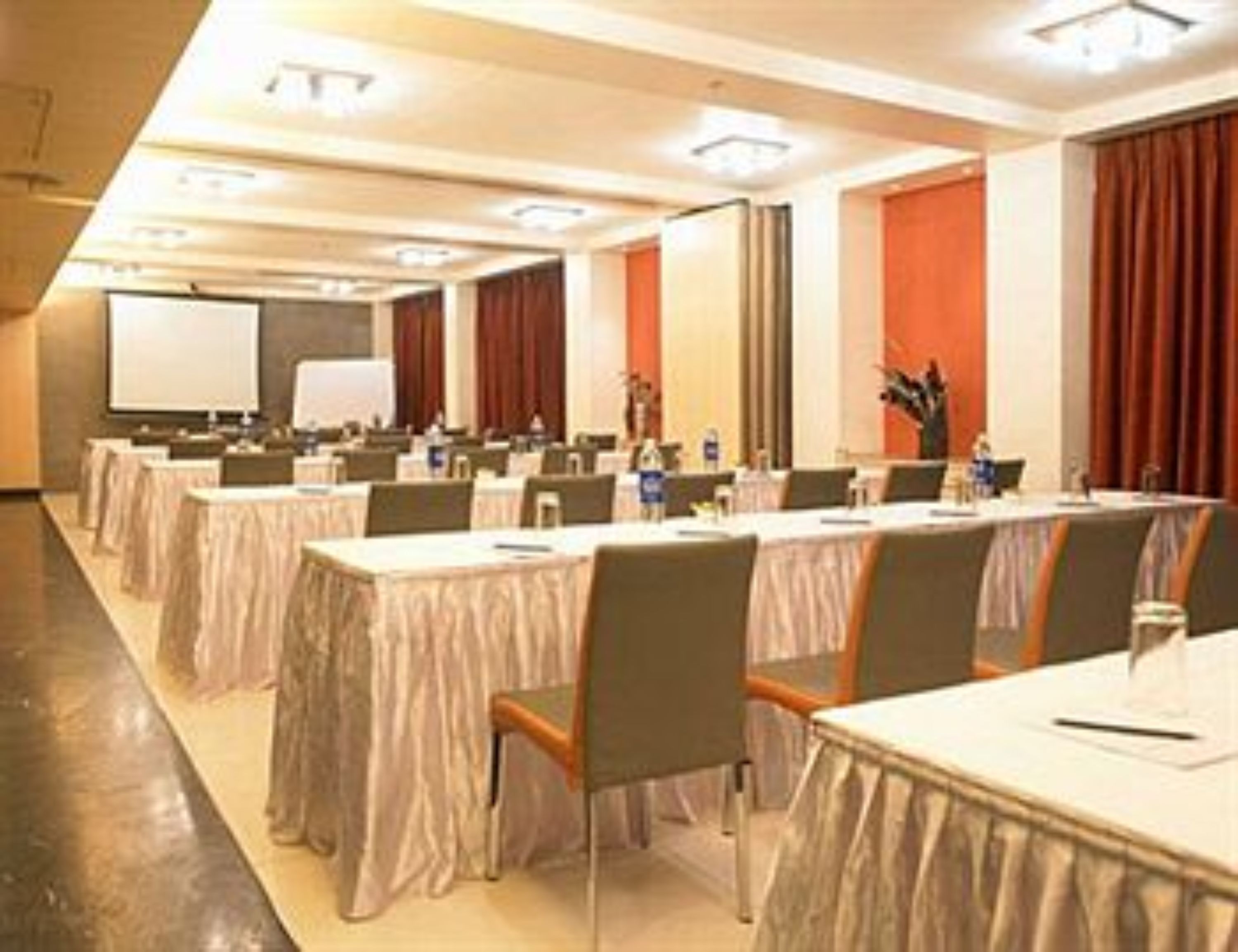 A conference room with multiple tables and chairs, a whiteboard, and a projector screen.