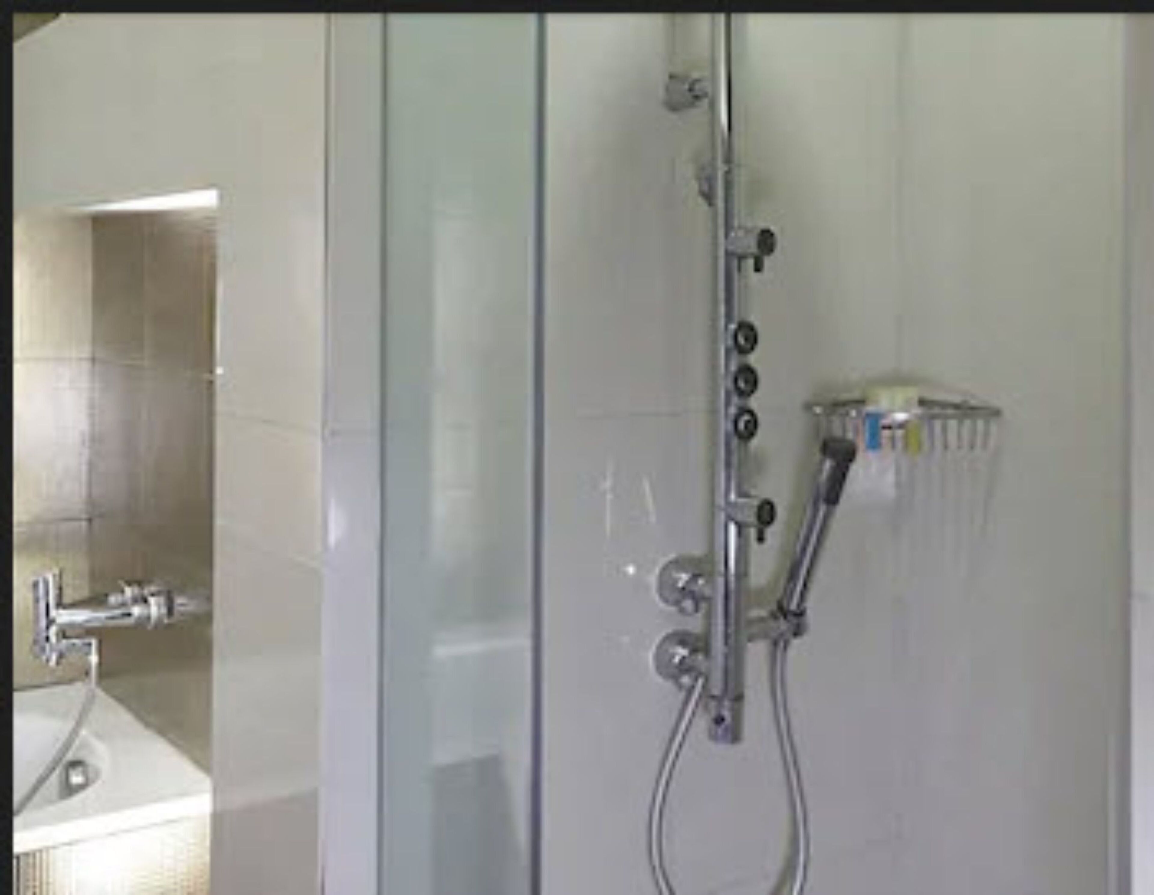 A glass-enclosed shower with a handheld showerhead and a wall-mounted faucet.