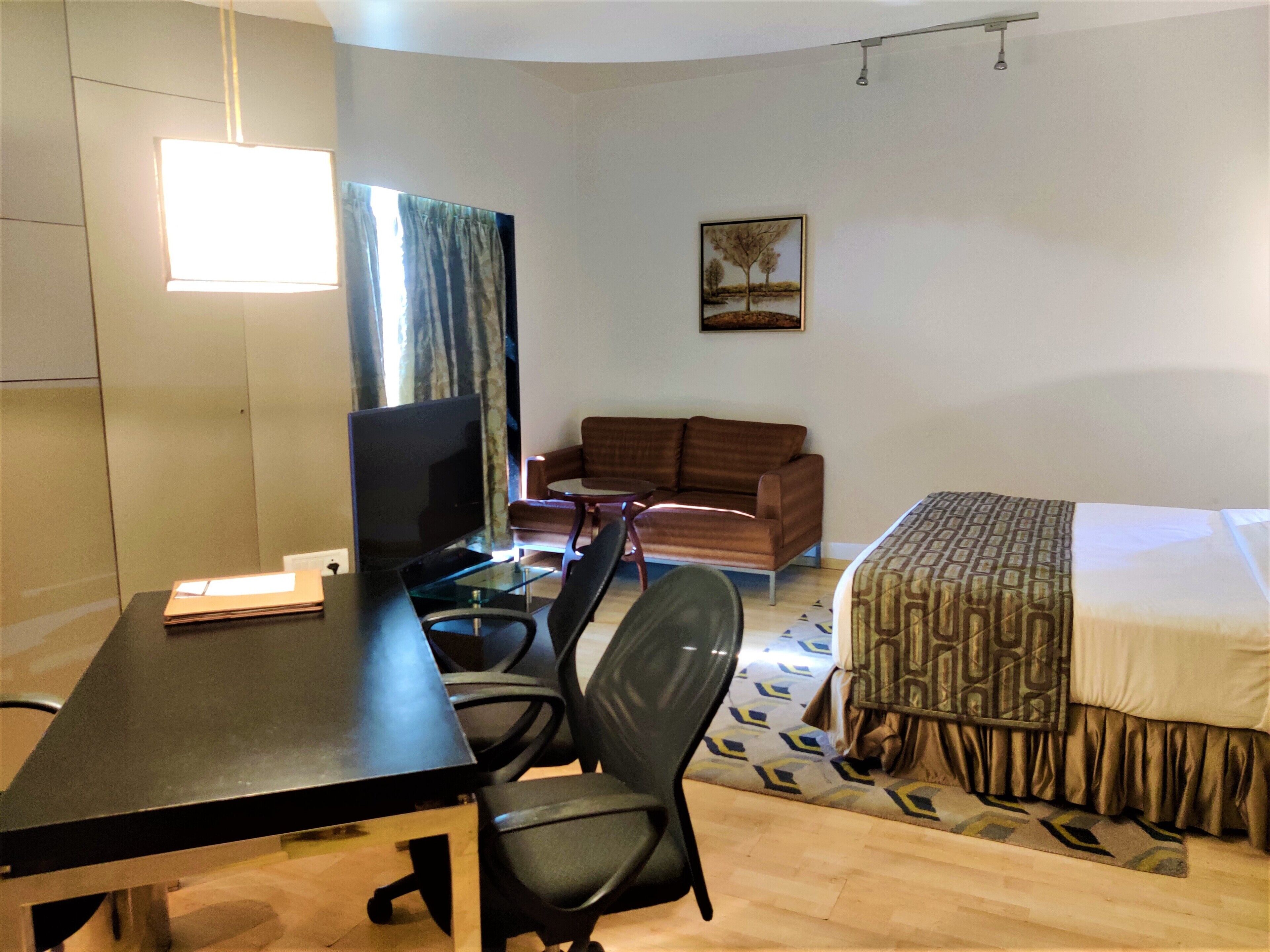 A hotel room with a bed, a sofa, a desk with a computer, and a TV.