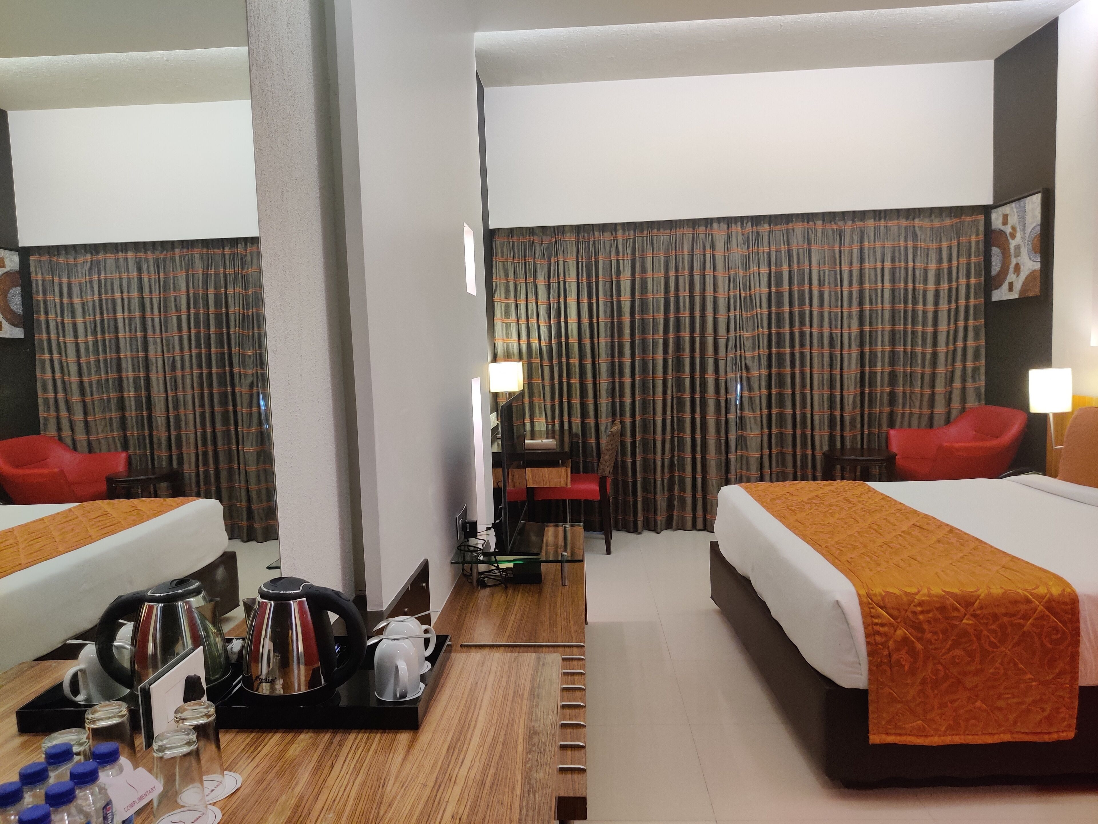 A hotel room with two beds, a desk, a chair, a red armchair, and a coffee station.