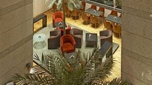 A modern indoor seating area with multiple tables and chairs, a large palm tree, and a view through large windows. - Hotel Satkar Residency (Thane)