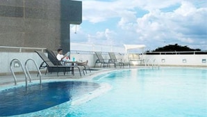 A swimming pool with lounge chairs and a person reading a book. - Hotel Satkar Residency (Thane)
