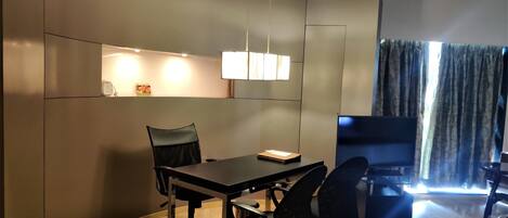 A modern living room with a curved wall, a dining area with a table and chairs, a flat-screen TV, and a large window with curtains.