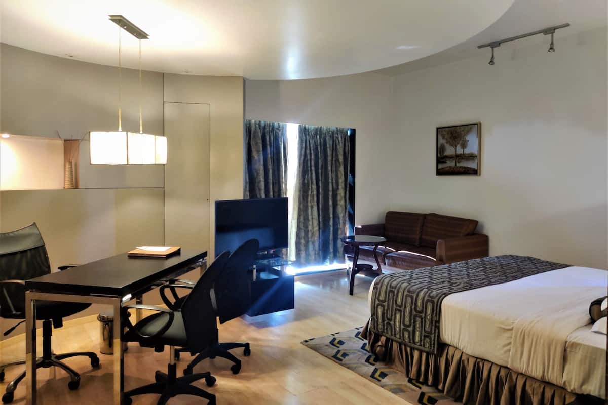 A hotel room with a desk, office chair, bed, and a television.