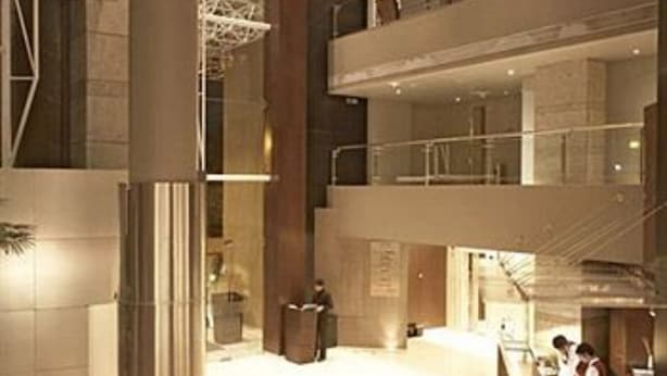 A modern hotel lobby with a central reception desk, a staircase, and a glass railing overlooking the lower level. - Hotel Satkar Residency (Thane)