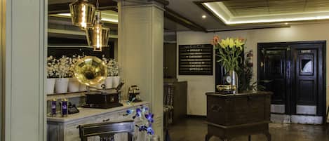 A dining area with a wooden table set for two, a gramophone, and a vase with flowers.