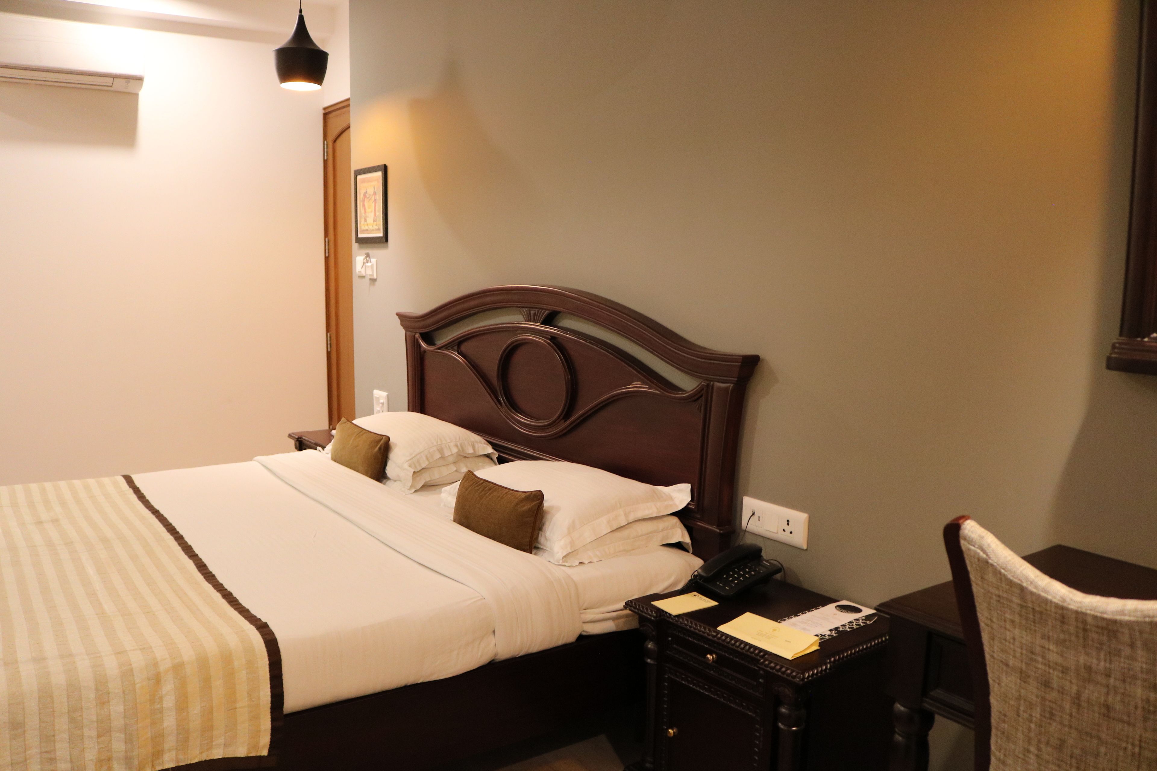 A neatly made bed with a wooden headboard, a bedside table with a lamp, and a chair.