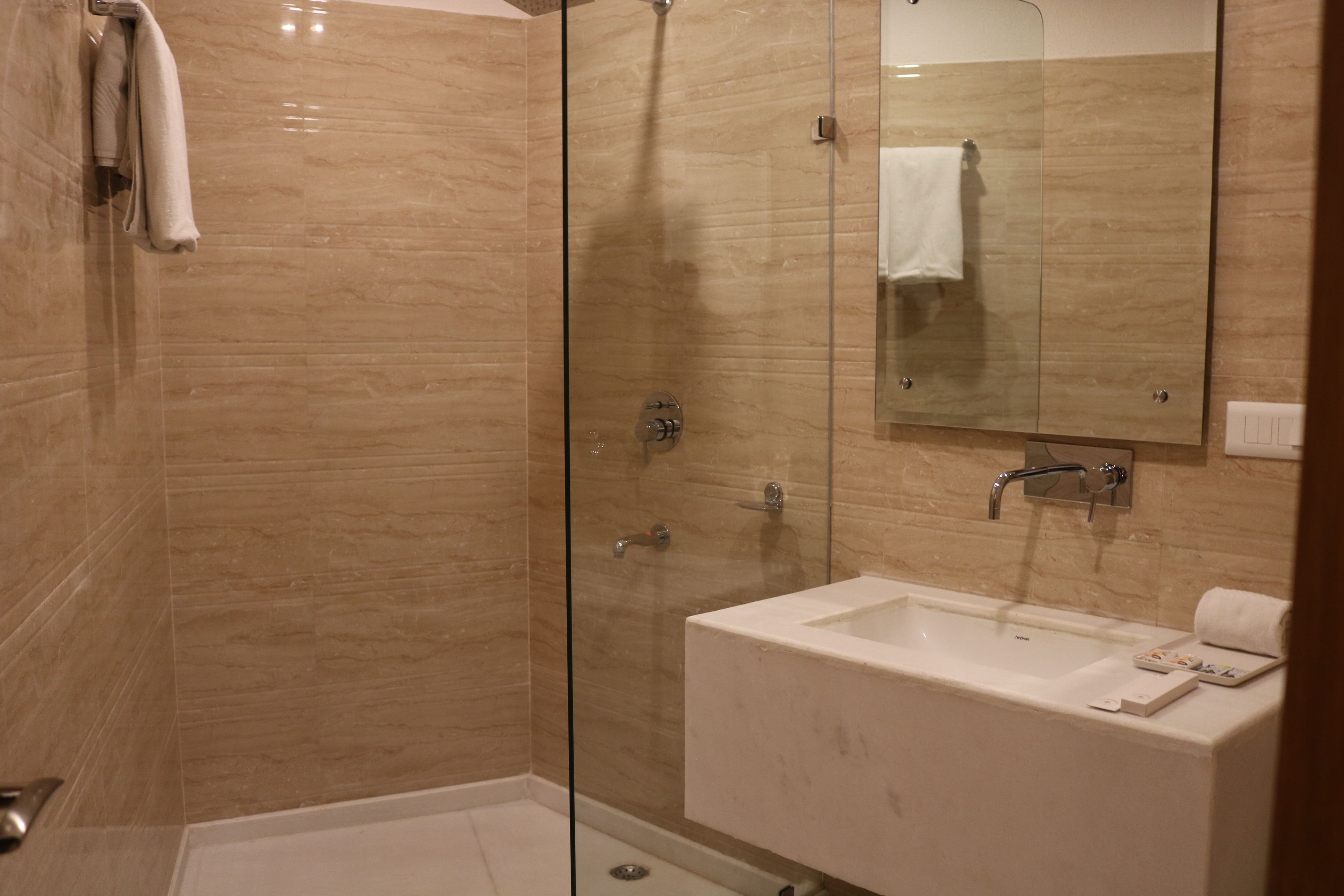 Ein modernes Badezimmer mit einer gläsernen Dusche, einem weißen Waschbecken und einem großen Spiegel.