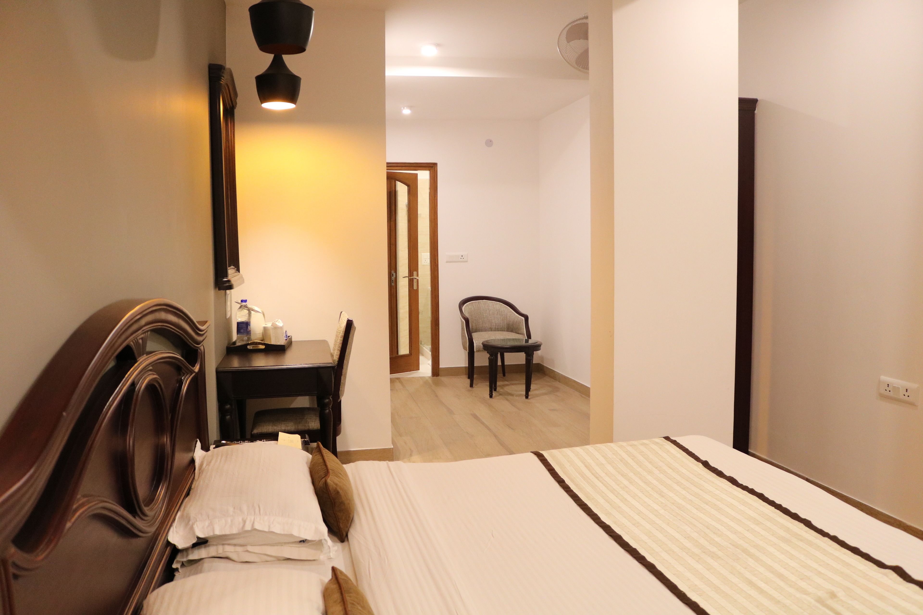 A hotel room with a bed, a desk with a chair, a mirror, and a door leading to another room.