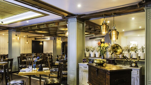 A restaurant with wooden tables and chairs, hanging pendant lights, and a bar area with a vintage counter. - Hotel Park Residency (New Delhi)