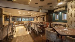 A restaurant with a modern interior, featuring a mix of wooden and upholstered furniture, a patterned wall, and a ceiling with recessed lighting. - Hotel Le Grande - Mumbai International Airport (Mumbai)