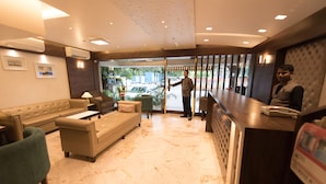 A hotel lobby with a reception desk, a sofa, a chair, and a coffee table. - Hotel Le Grande - Mumbai International Airport (Mumbai)