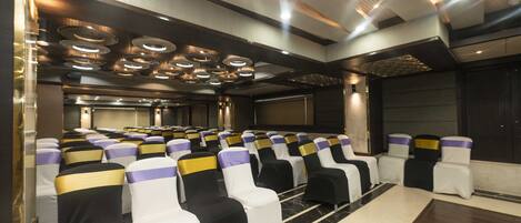 A conference room with rows of chairs, a stage, and a large screen.