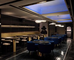 Un restaurante moderno con mesas redondas y sillas azules, que destaca por su interior oscuro e iluminación azul en el techo.