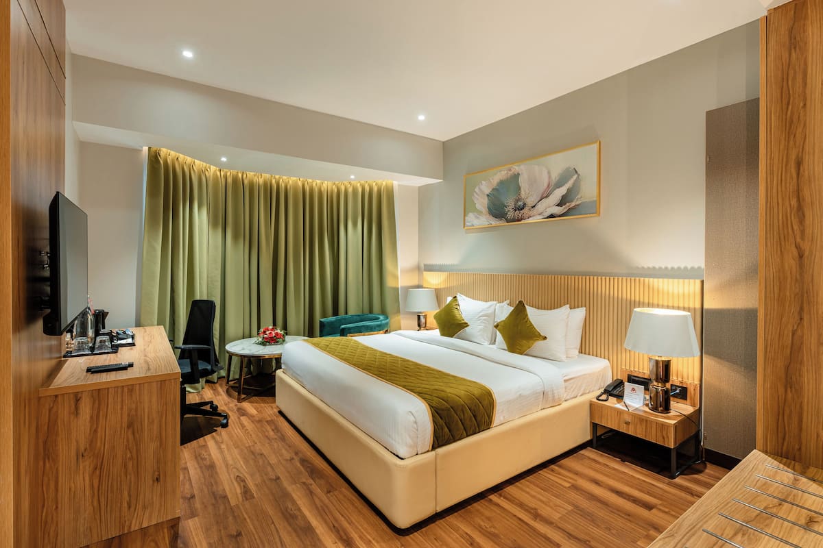 A hotel room with a bed, bedside table, lamp, chair, desk, and a television.