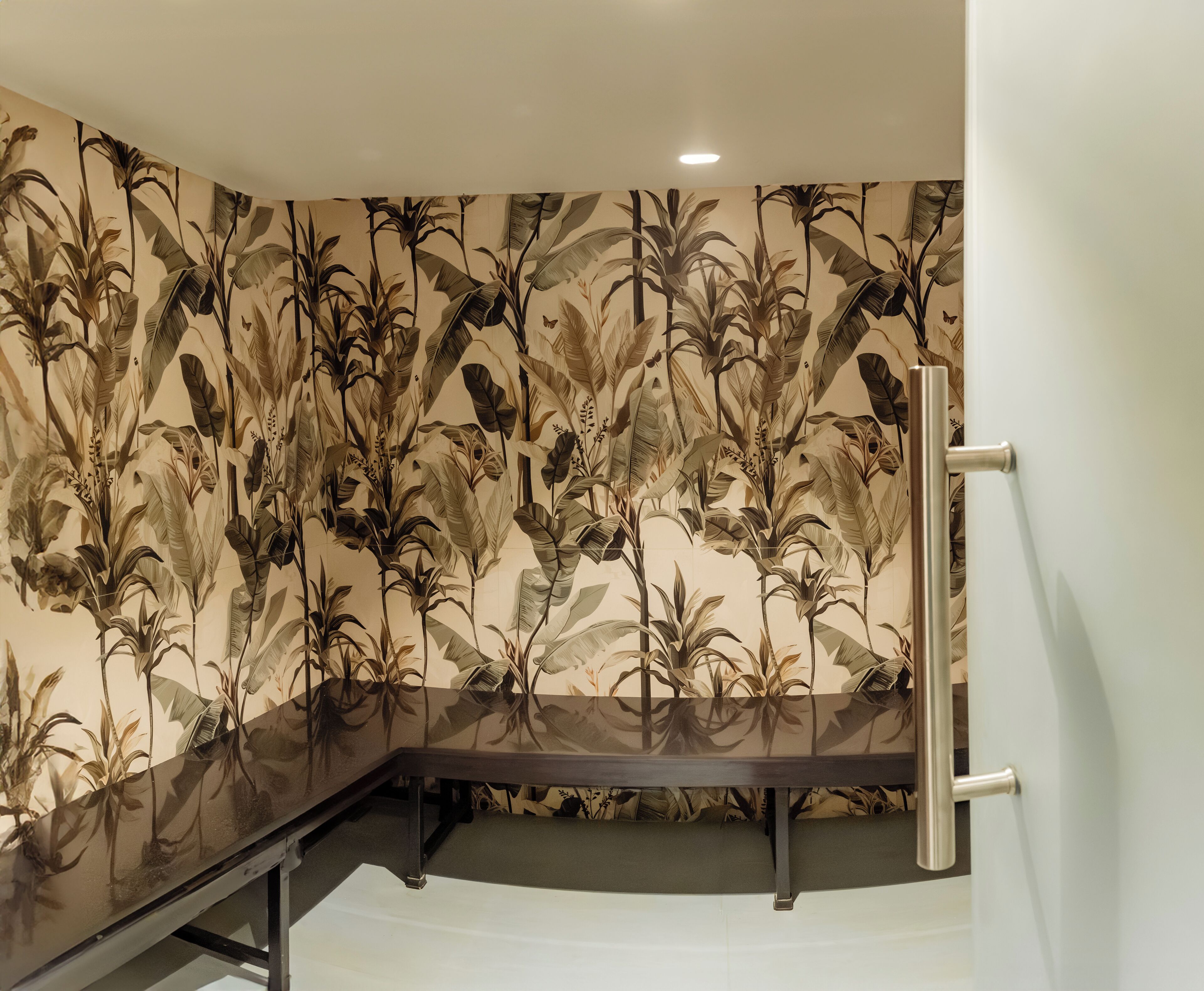Una habitación con un espejo grande, una banca y un papel tapiz de motivos vegetales tropicales.