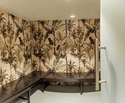 Una habitación con un espejo grande, una banca y un papel tapiz de motivos vegetales tropicales.