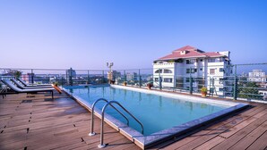 A rooftop pool with lounge chairs, a swimming pool, and a view of the cityscape. - Travancore Court (Kanayannur)