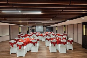 A conference room with rows of tables and chairs, each with red sashes, and a large screen at the front.