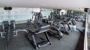 A modern gym with various cardio and strength training equipment, large windows, and a city view.