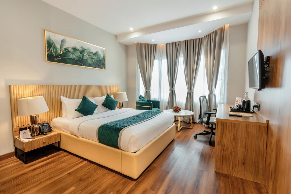 A modern hotel room with a large bed, bedside tables, a desk, a chair, and a TV.