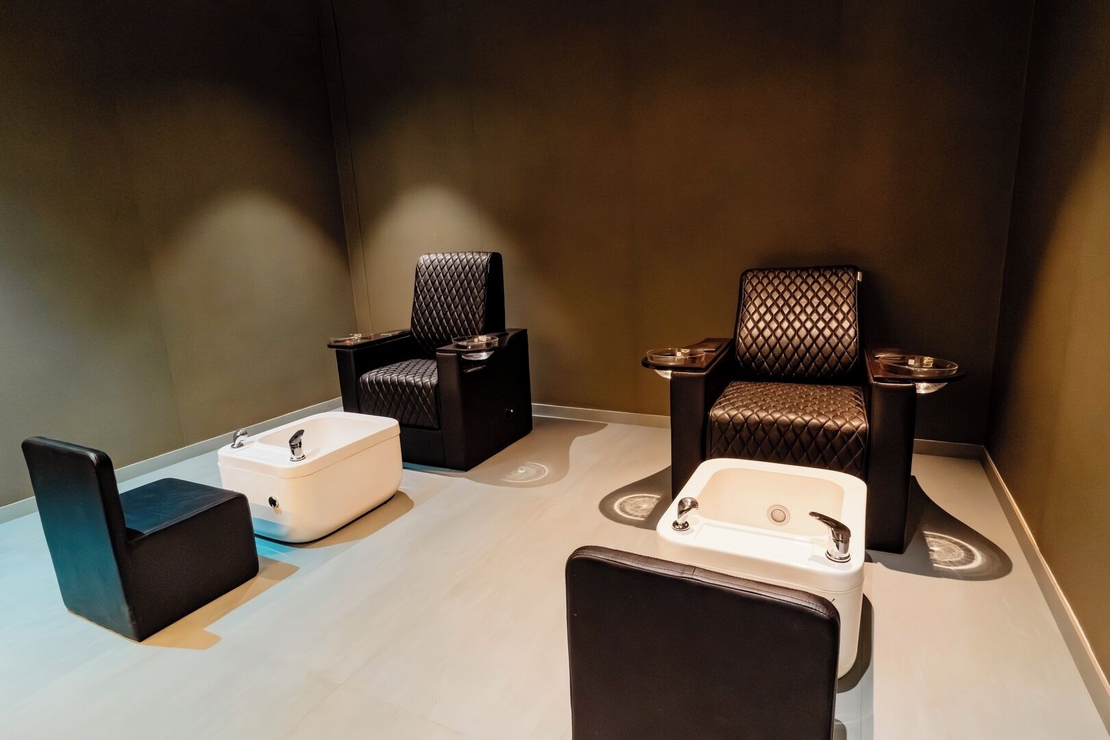 A spa room with two black leather chairs, a white massage table, and a small white sink.