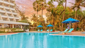 A pool area with lounge chairs and umbrellas, surrounded by palm trees and a hotel building. - The Resort Mumbai (Mumbai)