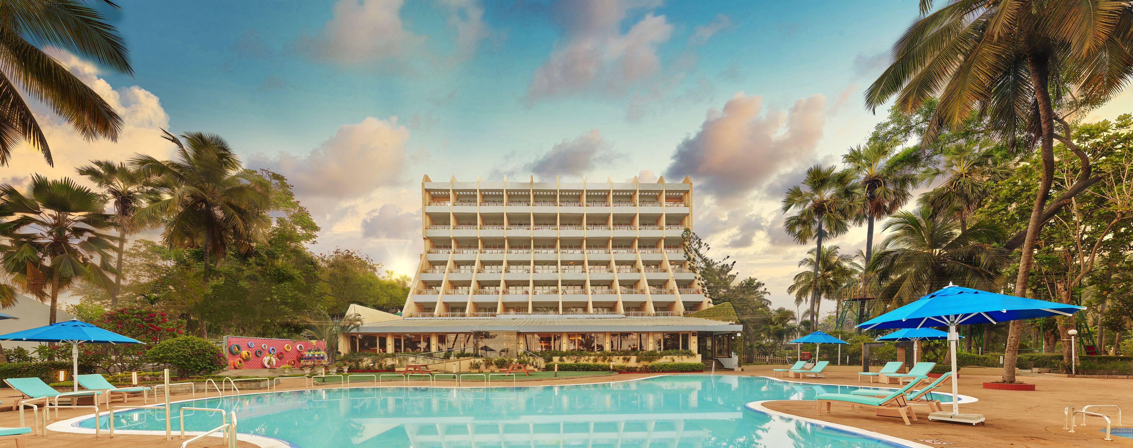 A hotel with a pool, palm trees, and a large building with multiple balconies.