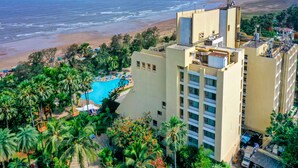 A hotel with a pool surrounded by palm trees, a beach view, and a high-rise building with balconies. - The Resort Mumbai (Mumbai)