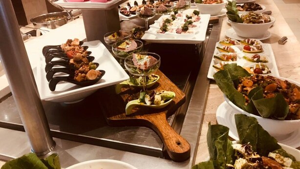 Un bufé con diversos platos, incluyendo ensaladas, carnes y postres, dispuestos en múltiples fuentes.