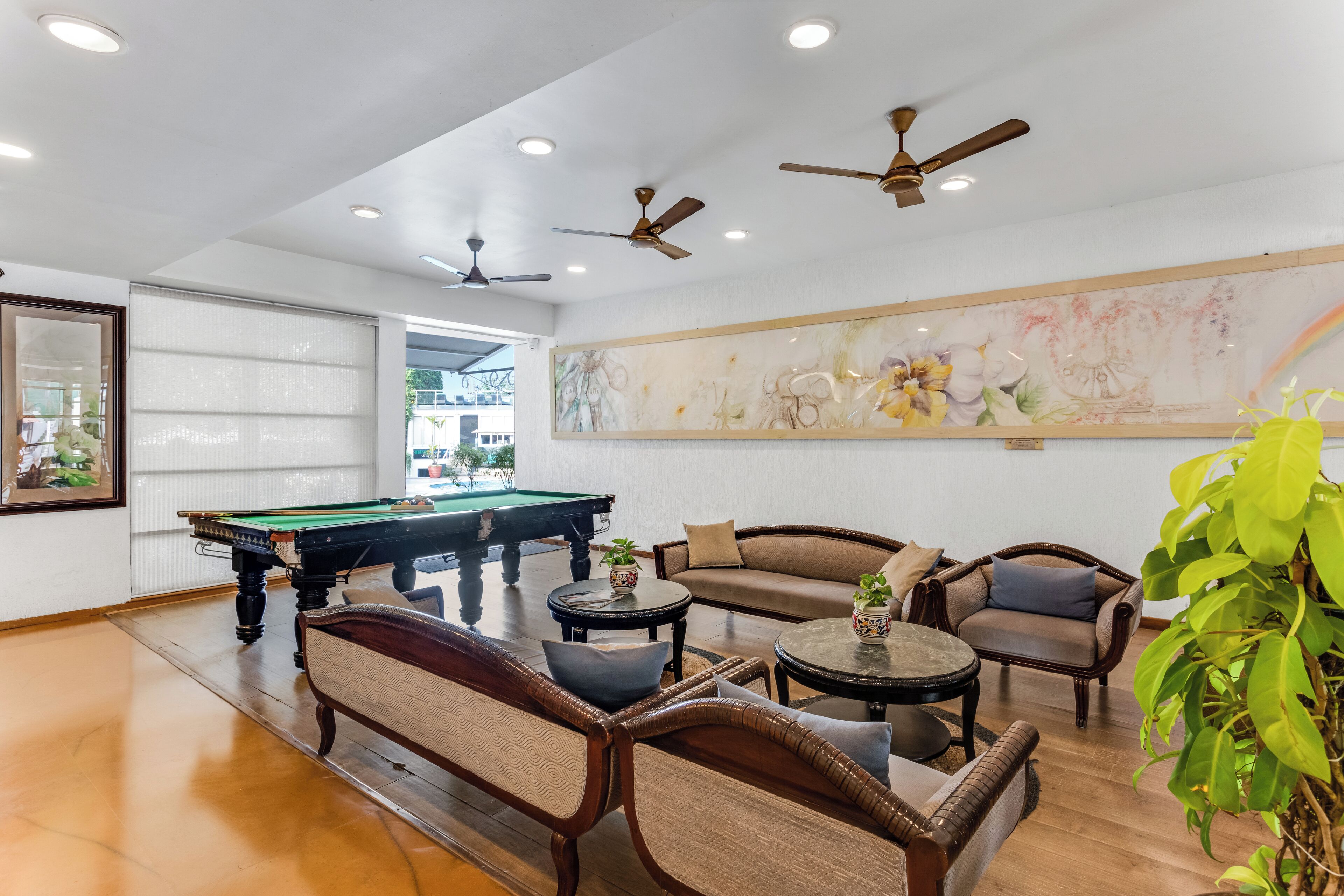 A billiards room with a pool table, cushioned seating, ceiling fans, and a large abstract painting on the wall.