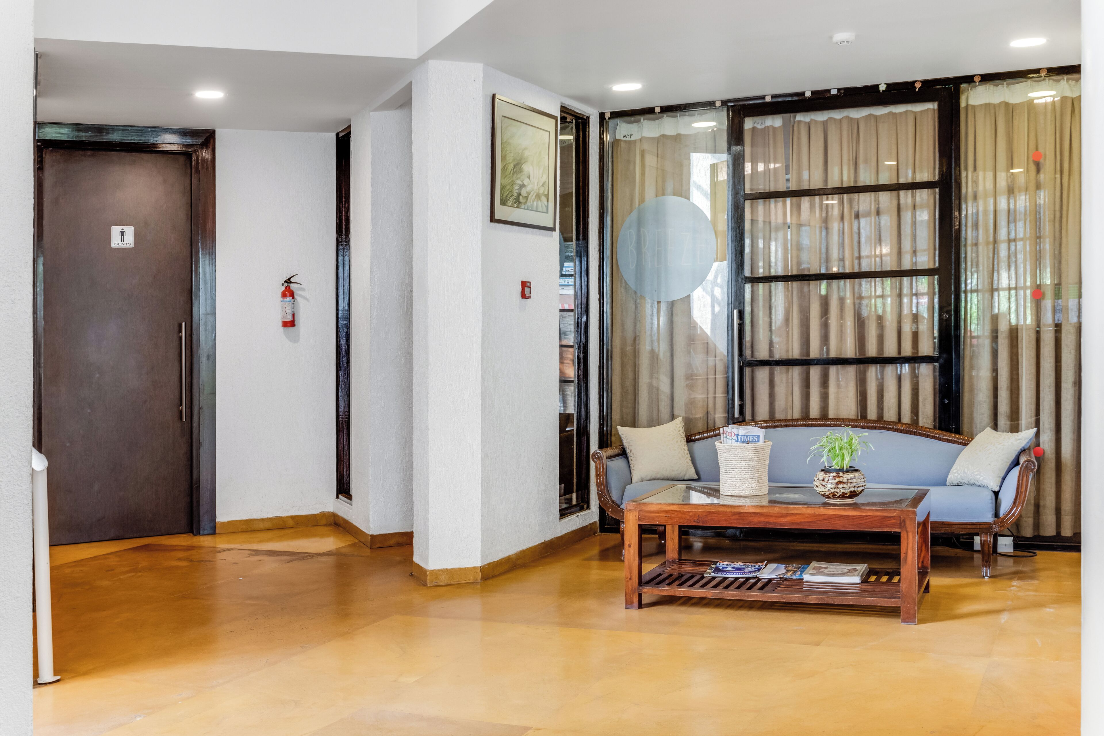 A lobby with a wooden floor, a sofa with cushions, a coffee table, and a fire extinguisher on the wall.