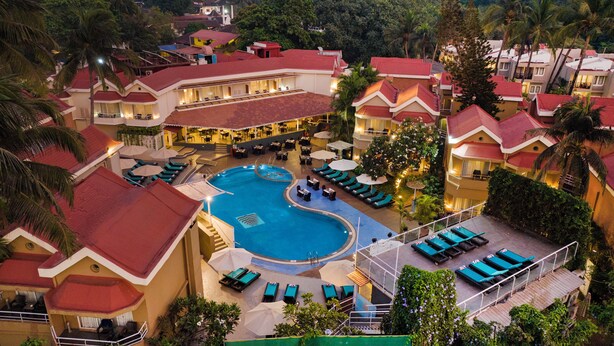 A resort with a central swimming pool, multiple lounge areas, and a variety of accommodations with red-tiled roofs. - Whispering Palms Beach Resort (Candolim)