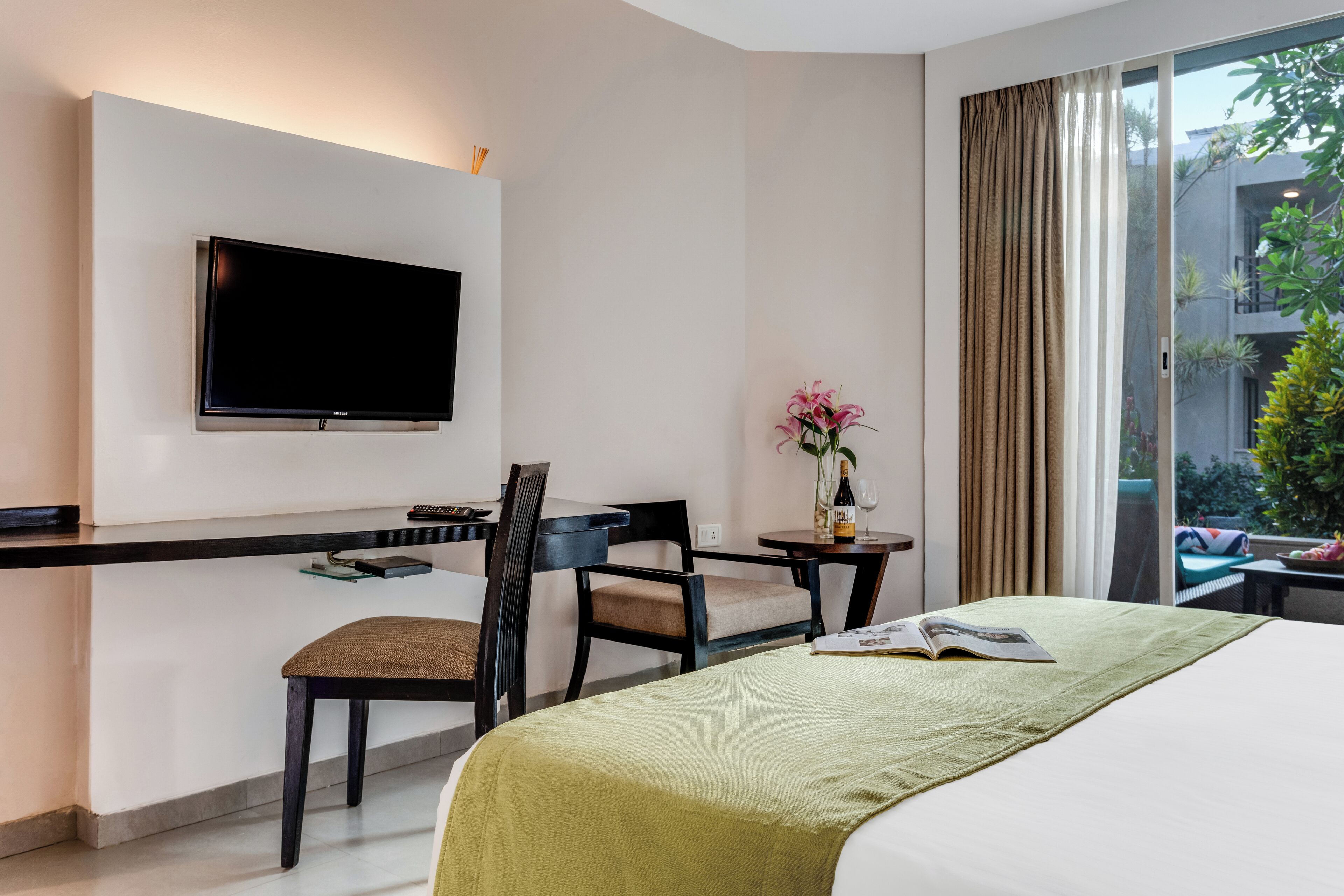 A hotel room with a bed, a desk with a chair, a television mounted on the wall, and a window with curtains.