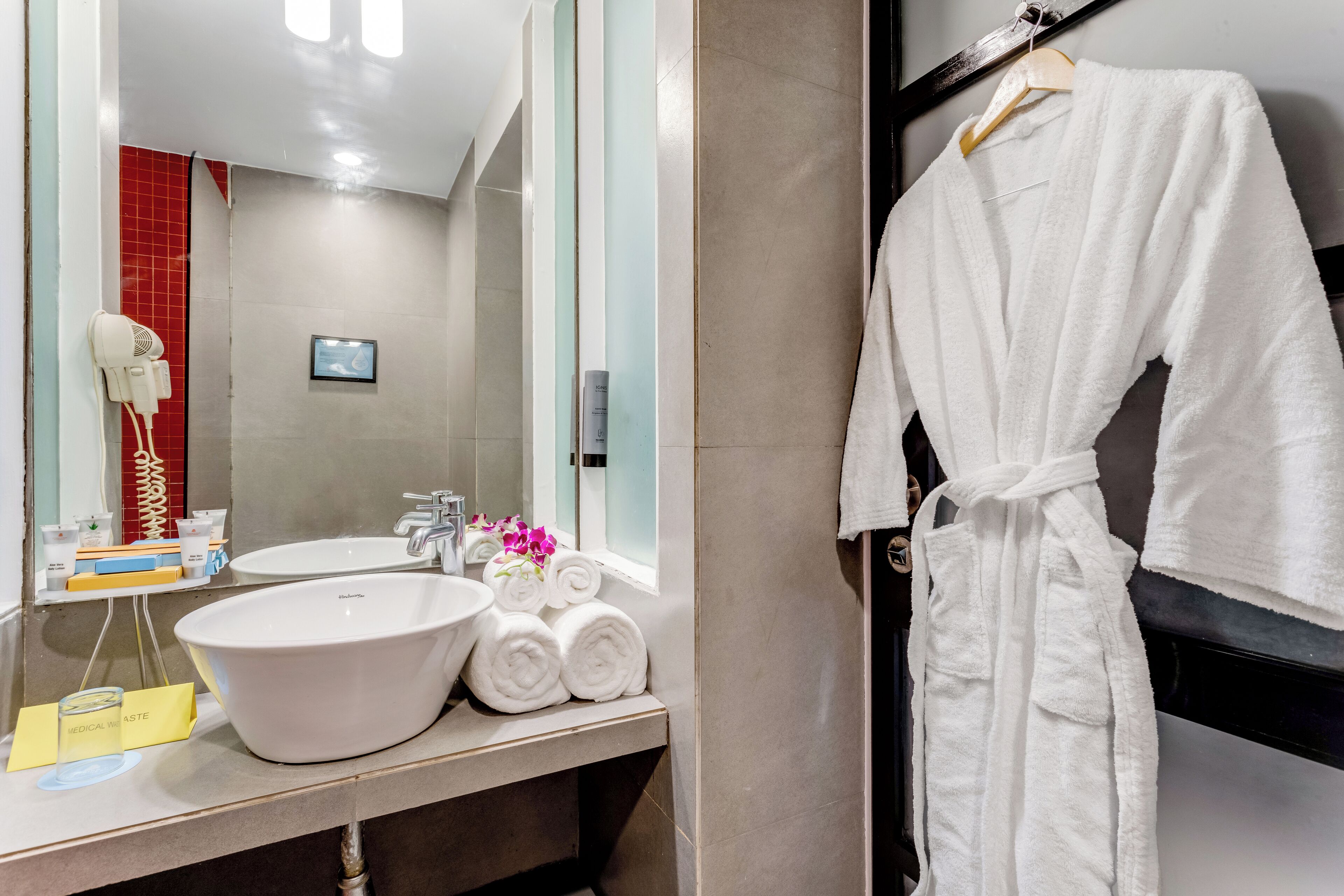 A bathroom with a large sink, a mirror, a hairdryer, and a robe hanging on a rack.
