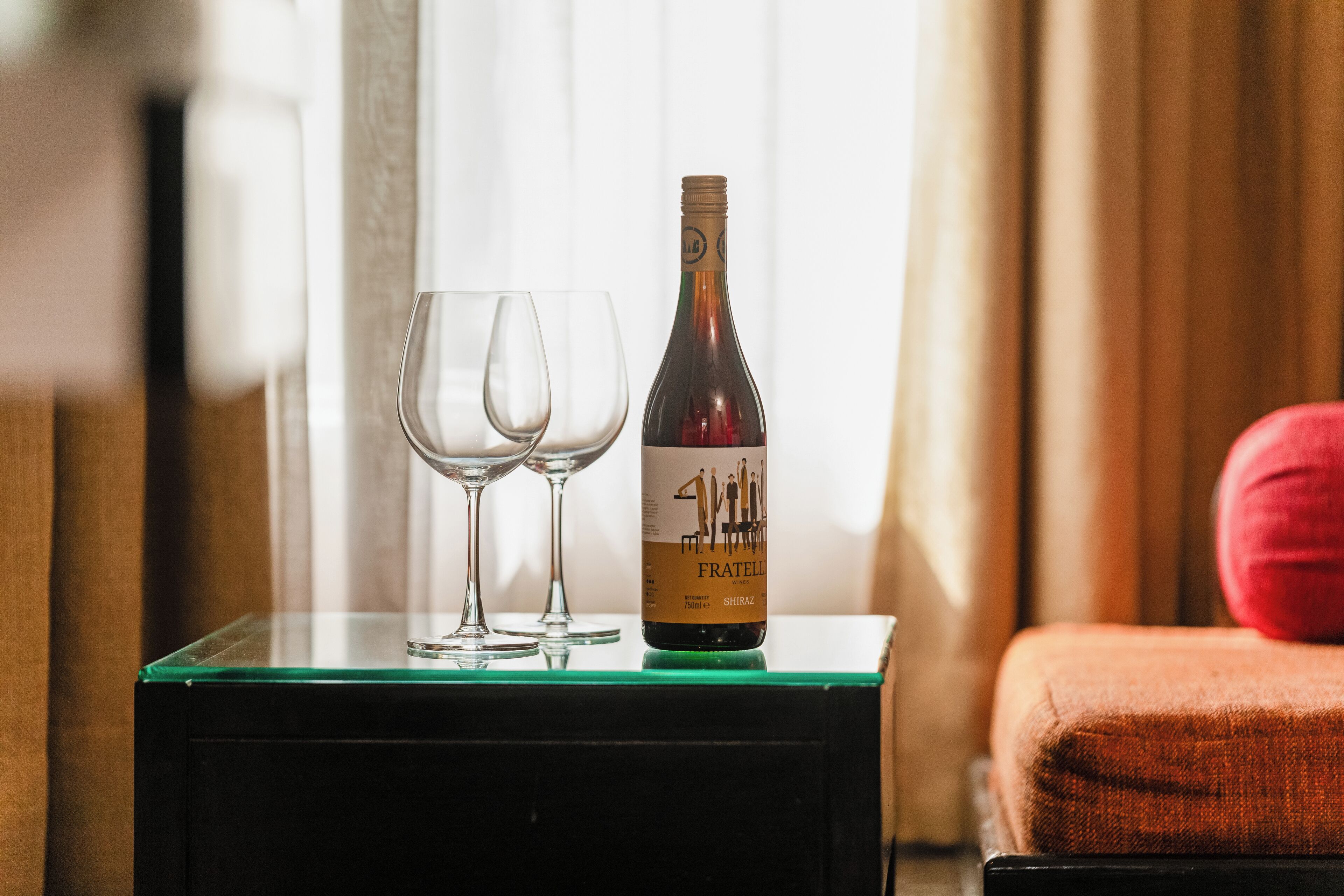 Una botella de vino Fratelli Shiraz y dos copas de vino vacías sobre una mesa de vidrio.