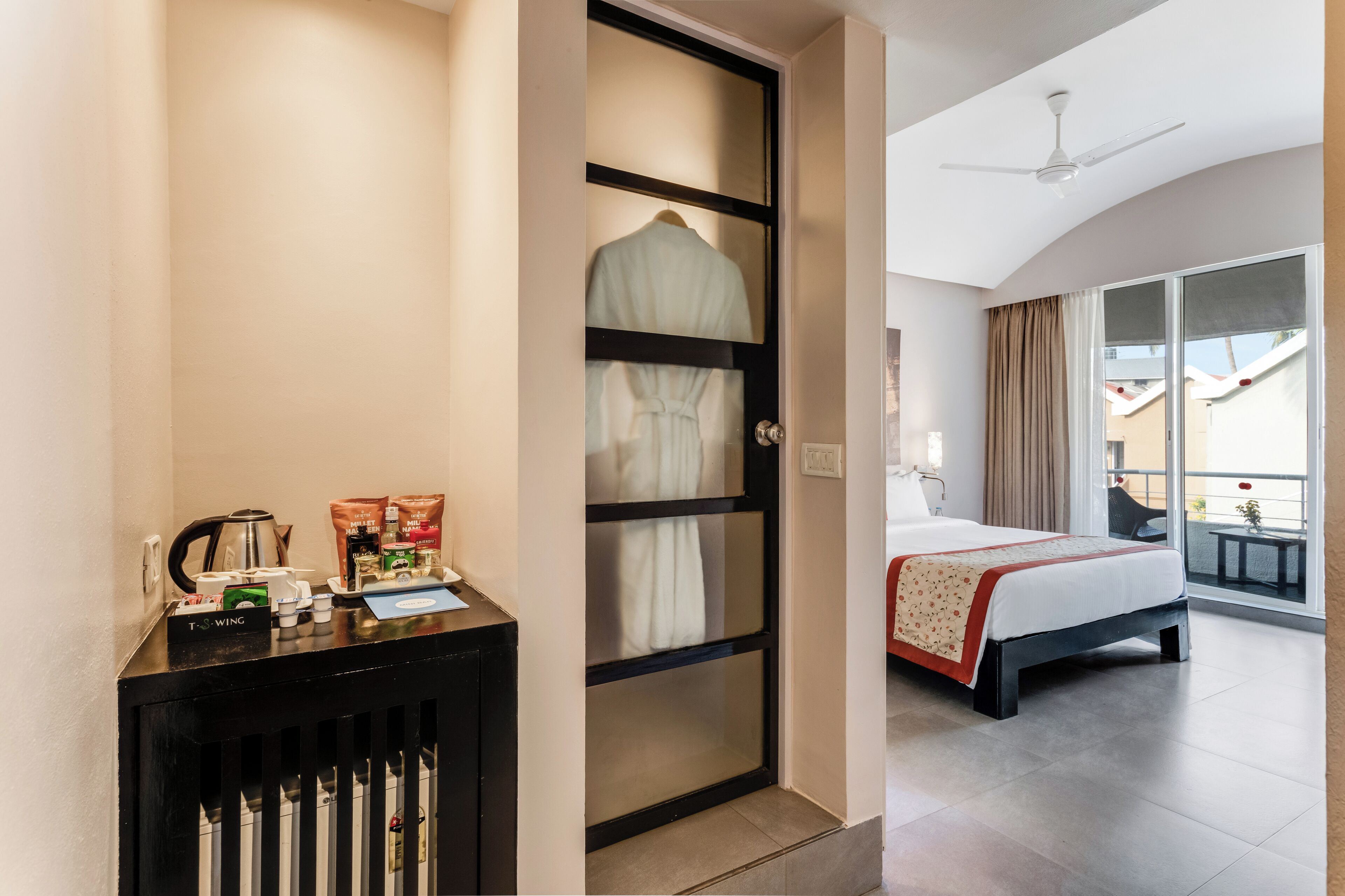 Quarto de hotel com uma cama, uma escrivaninha com produtos de higiene, um roupão pendurado na porta e uma varanda com vista.