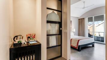 Quarto de hotel com uma cama, uma escrivaninha com produtos de higiene, um roupão pendurado na porta e uma varanda com vista.