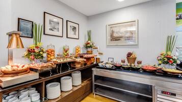 Zona de bufé con diversas opciones de comida, un aviso sobre alergias alimentarias y cuadros en la pared.