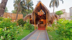 A thatched-roof structure with a red carpet leading to the entrance, surrounded by lush greenery and palm trees. - Whispering Palms Beach Resort (Candolim)