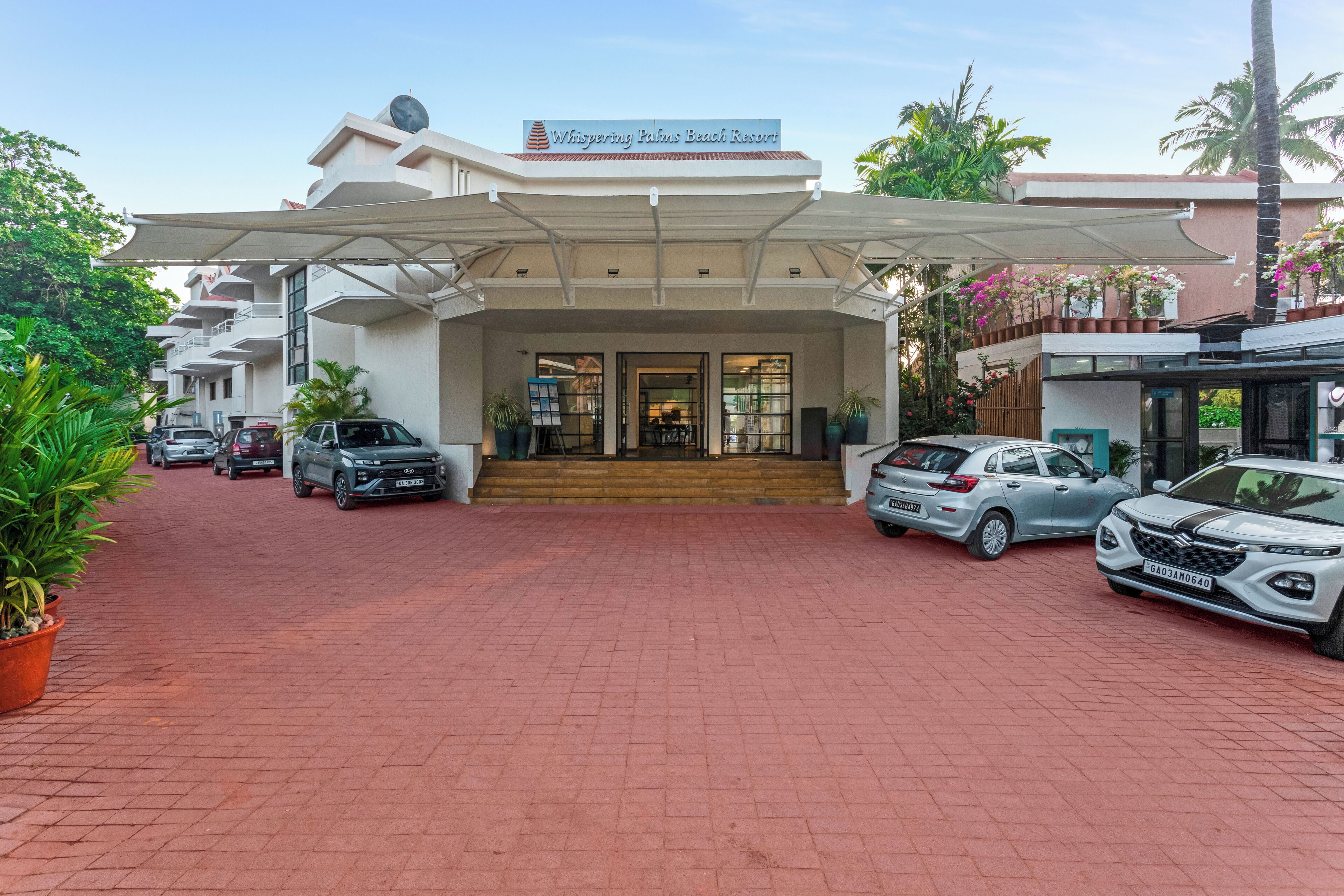 A hotel entrance with a covered walkway, parked cars, and potted plants.