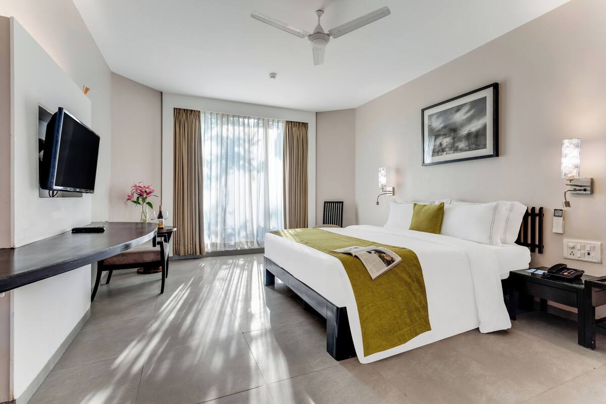 A modern hotel room with a bed, desk, television, and a painting on the wall.