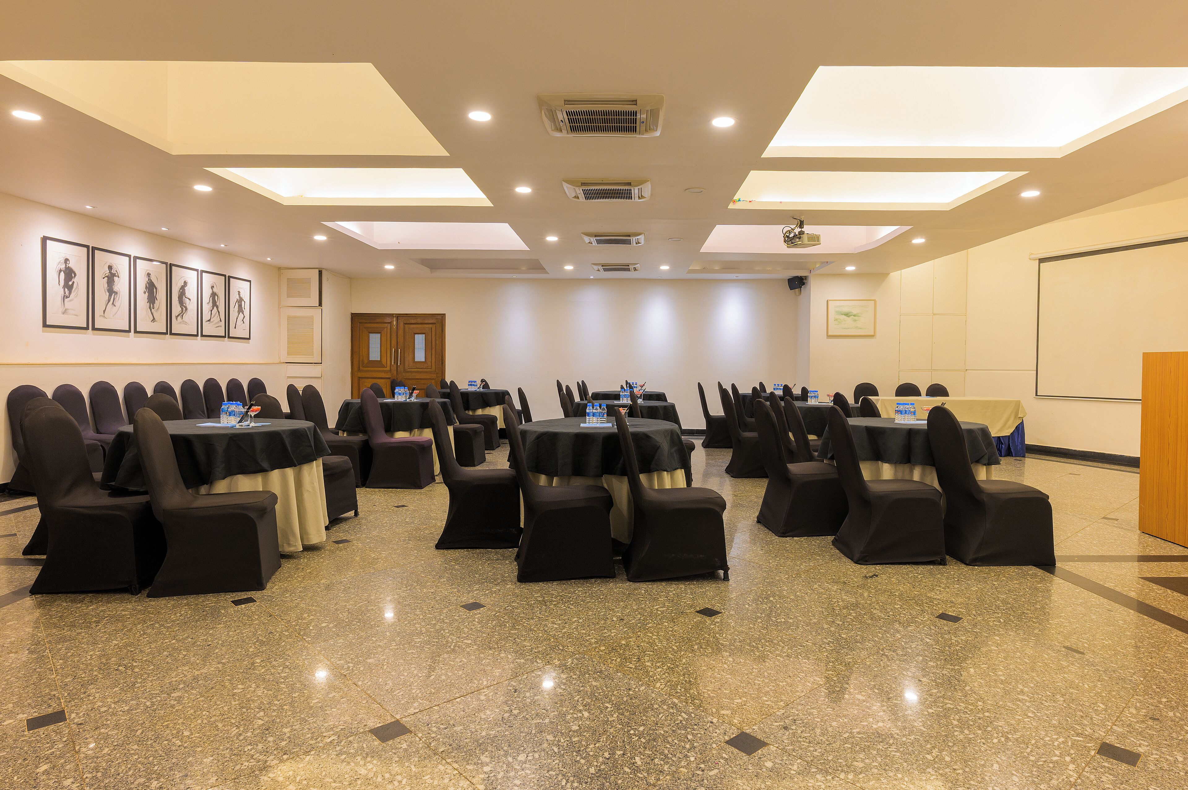 Un salón de conferencias con varias mesas y sillas, equipado con proyectores y pantallas.