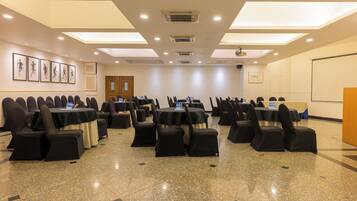 Un salón de conferencias con varias mesas y sillas, equipado con proyectores y pantallas.