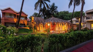 A resort with a thatched-roof structure, surrounded by lush greenery and palm trees. - Whispering Palms Beach Resort (Candolim)